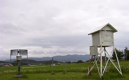 Garita meteorológica en un emplazamiento abierto en Kvithamar, Noruega, sobre terreno con hierba corta; pluviómetro a la izquierda